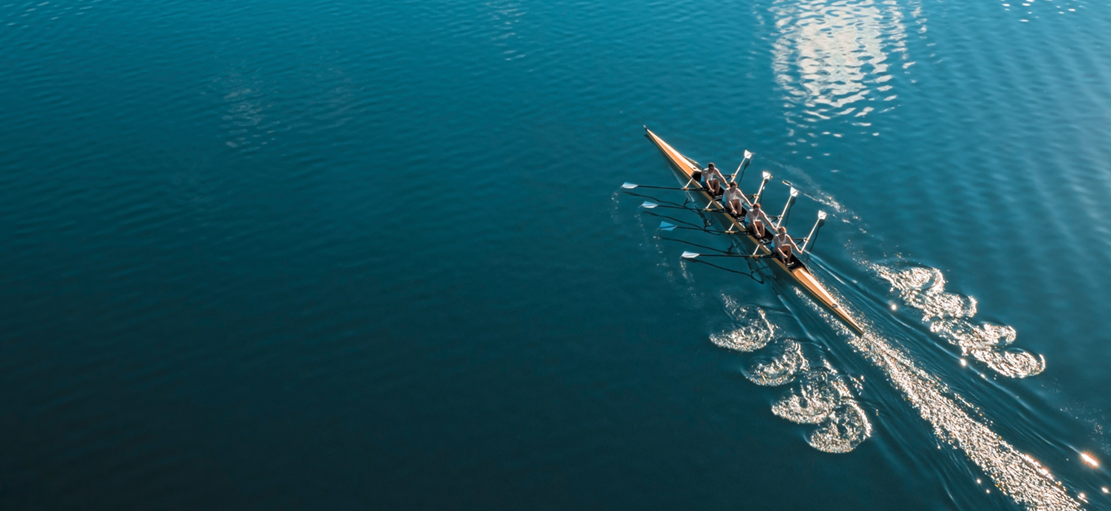 Image of clear blue water and a rowing team paddling in sync